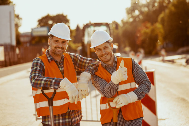 Two construction workers in hardhats and vests posing for a photo at the road - Zdjęcie, obraz