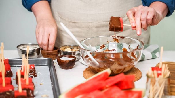 Εμβάπτιση κύβους καρπούζι σε λιωμένη σοκολάτα και γαρνίρισμα με θαλασσινό αλάτι και αμύγδαλα. - Φωτογραφία, εικόνα