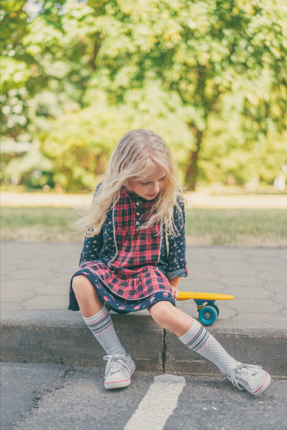 little child sitting on skateboard at urban street - Foto, afbeelding