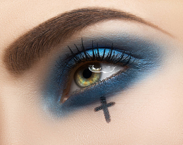 Macro y primer plano creativo maquillaje tema: hermoso ojo femenino con sombras de ojos azules y dibujo cruz, halloween
 - Foto, imagen