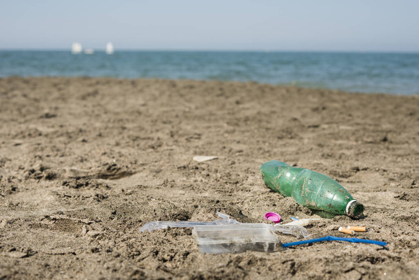 Green, plastic bottle, cotton swabs, cap, box and cigarettes left on a sandy beach. - Foto, afbeelding