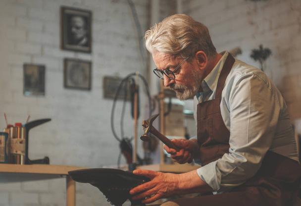 An elderly shoemaker at work in the workshop - Foto, imagen