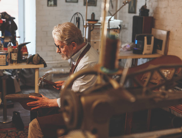 Un zapatero de edad avanzada trabajando en el taller
 - Foto, Imagen