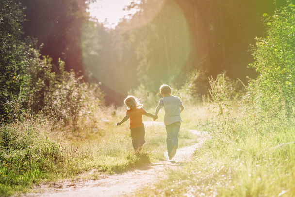 χαρούμενο μικρό αγόρι και κορίτσι τρέχουν στο ηλιοβασίλεμα της φύσης - Φωτογραφία, εικόνα