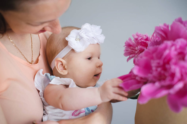 Щаслива молода мама обіймає новонароджену дитину і допомагає досліджувати світ, показуючи букет квітів
 - Фото, зображення