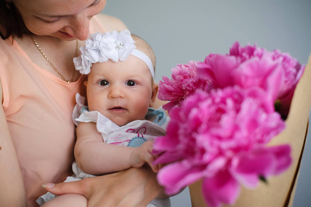 Ευτυχισμένος νέος μητέρα αγκαλιάζει το νεογέννητο παιδί της και να εξερευνήσετε τον κόσμο που δείχνουν μπουκέτο με λουλούδια - Φωτογραφία, εικόνα