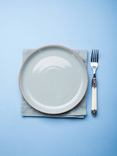 Синя пастельна керамічна тарілка на серветці з виделкою
 - Фото, зображення