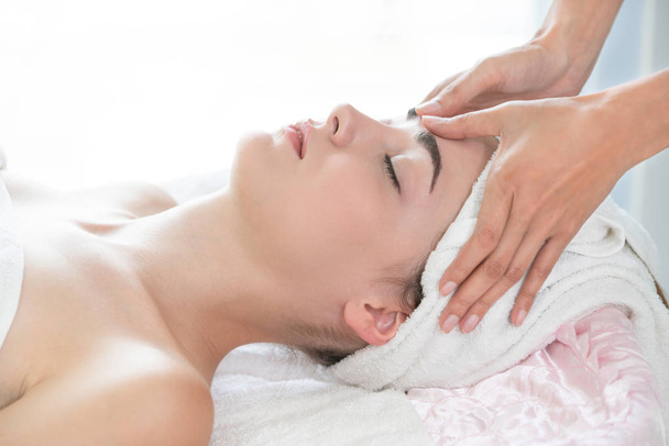 Relaxed woman lying on spa bed for facial and head massage spa treatment by massage therapist in a luxury spa resort. Wellness, stress relief and rejuvenation concept. - Photo, image