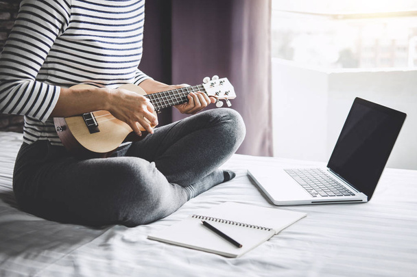 Young happiness woman on bedroom in enjoying playing the music with guitar or ukulele in holiday, relaxation and recreation concept. - Foto, Imagem