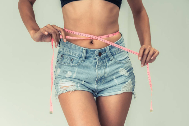 Young slim woman measures her waist by measuring tape after diet against white backgrounds. Concept of weight loss success. - Fotografie, Obrázek