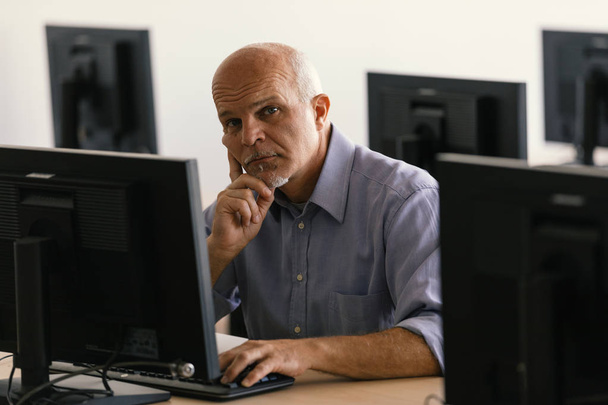 Uomo d'affari guardando la fotocamera mentre si lavora via sul computer desktop in classe impostazione
. - Foto, immagini