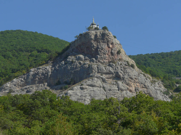 Церковь с черно-золотыми куполами на вершине горы посреди леса
 - Фото, изображение