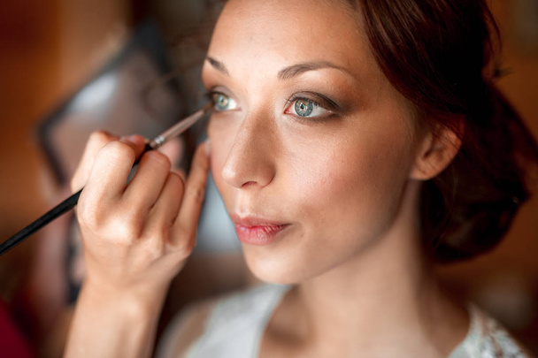 Proces van het maken van de make-up. Visagist bezig met borstel model gezicht. Portret van jonge brunette vrouw in beauty salon interieur - Foto, afbeelding