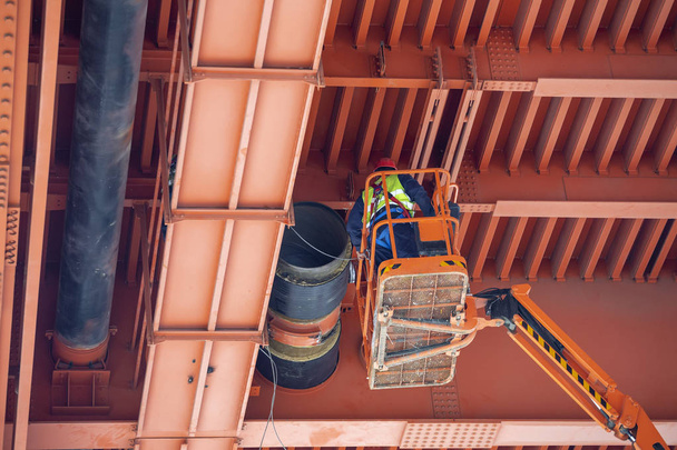 Travailleurs installant des tuyaux de chauffage urbain sous un pont métallique. Travaux d'installation de grands pipelines
. - Photo, image
