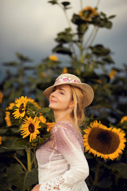 Beautiful woman in a rural field scene outdoors, with sunflowers and sunhat, lust for life, summerly, autumn mood  - Foto, imagen