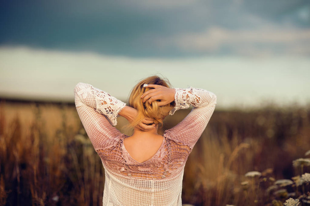 Beautiful blonde woman with long hair standing in a rural flower field outdoors, raising her hair, lust for life, summerly, autumn mood, view from her back - Foto, imagen