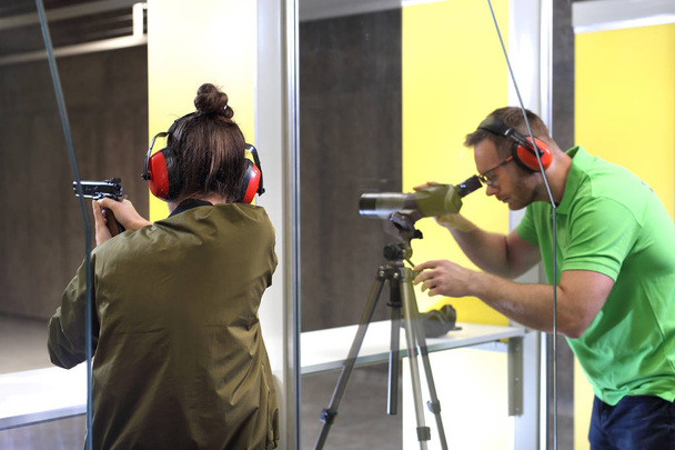 Recreational shooting at the shooting range. The woman shoots from the gun at the shooting range under the supervision of an instructor. - Zdjęcie, obraz