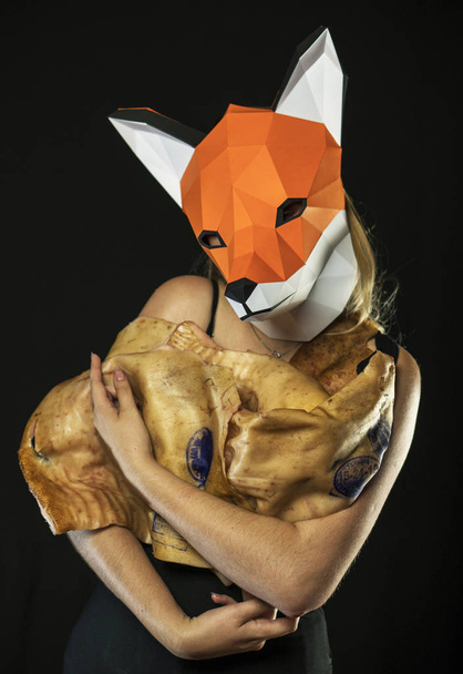 Ξανθιά κοπέλα με μάσκα αλεπούς χαρτί χρησιμοποιώντας δέρμα χοίρου για κάλυψη. Νεκροί ζωικοί καταναλωτή - Φωτογραφία, εικόνα