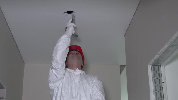 Trabajador profesional en desgaste de trabajo hacer agujeros de techo de paneles de yeso para instalar la luz
 - Imágenes, Vídeo
