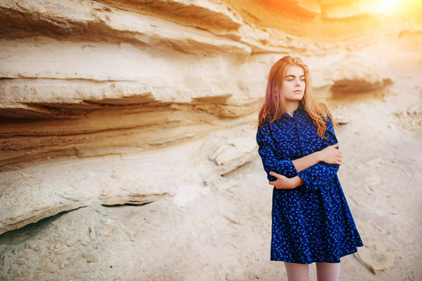 砂の採石場の真ん中に青いドレスを着て立っている美しい赤毛の少女. - 写真・画像