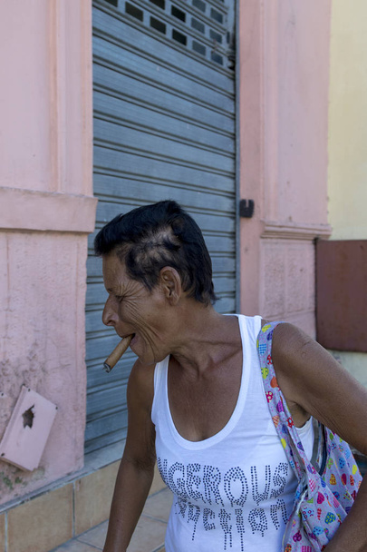 Havana Cuba Feb 11 2018: Unidentified lady smoking a cigar in the residential neighborhood in Havana. Cigar is the national smoke for many Cubans. - Photo, Image