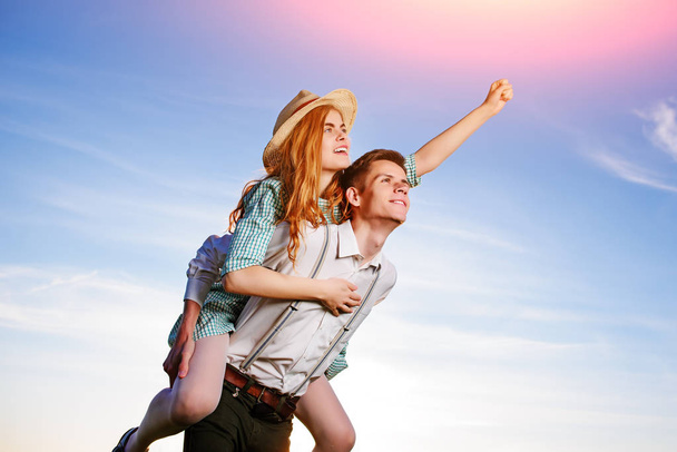 Young man piggybacking his happy girlfriend with raised hand. Cheerful lovers dreaming. - Photo, Image