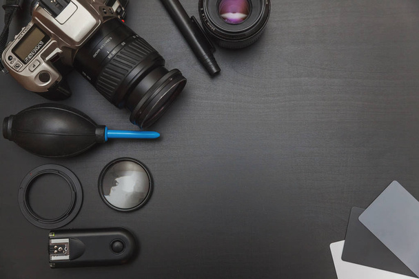 κάτοψη του φωτογράφου χώρο εργασίας με dslr κάμερα σύστημα, κιτ καθαρισμού κάμερας και εξάρτημα κάμερας σε τραπέζι μαύρο φόντο με αντίγραφο χώρου - Φωτογραφία, εικόνα