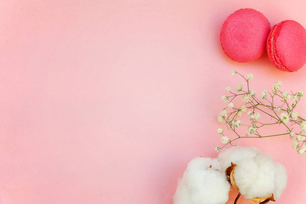 Вид сверху на мини-розовый макарон или макарон на французском десертном торте с хлопковыми цветками на мягком сладко-розовом бумажном плоском фоне
. - Фото, изображение