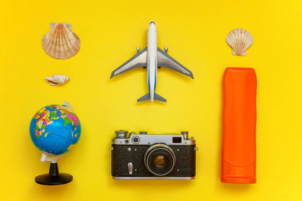 Flat Lay with sunscreen, plane, vintage camera, passport, globe, sunglasses and shell on yellow colourful trendy modern fashion background. Vacation travel summer weekend sea adventure trip concept - Photo, Image