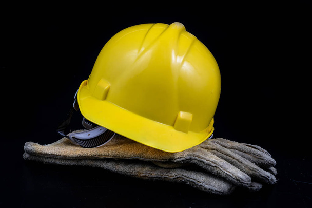 Helmet and workwear on a black working table. Accessories for construction workers. Black background. - Foto, Imagen