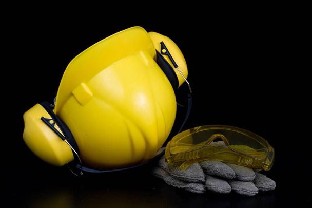 Helmet and workwear on a black working table. Accessories for construction workers. Black background. - Foto, imagen