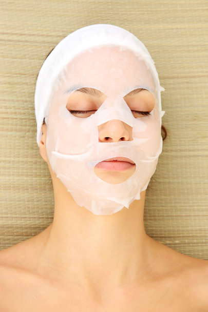 Young woman with cloth facial mask, on bamboo mat background - Foto, Imagen