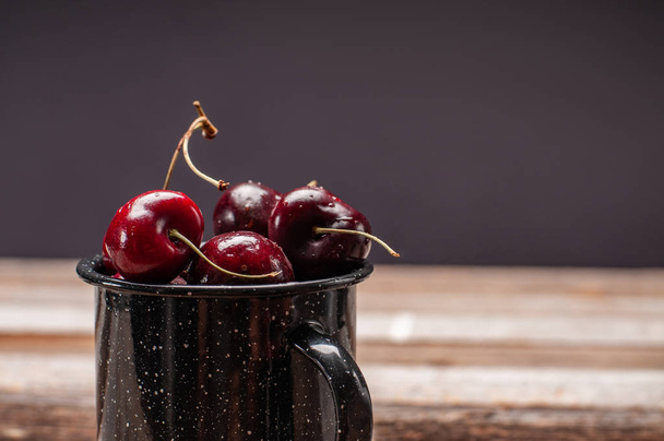 Fresh ripe cherries. Cherries in the enameled cup on wooden table  - Photo, Image