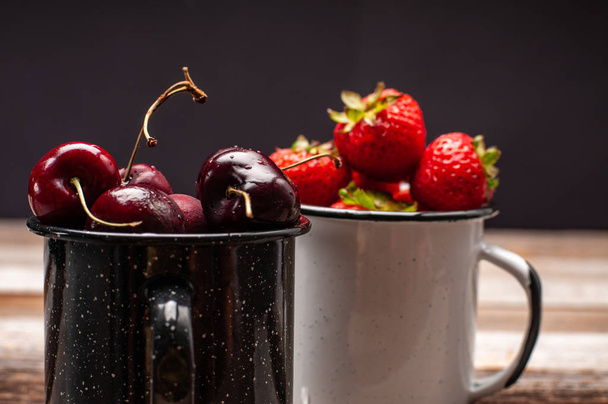 Bagas maduras frescas. Cerejas e morangos no copo esmaltado na mesa de madeira
  - Foto, Imagem