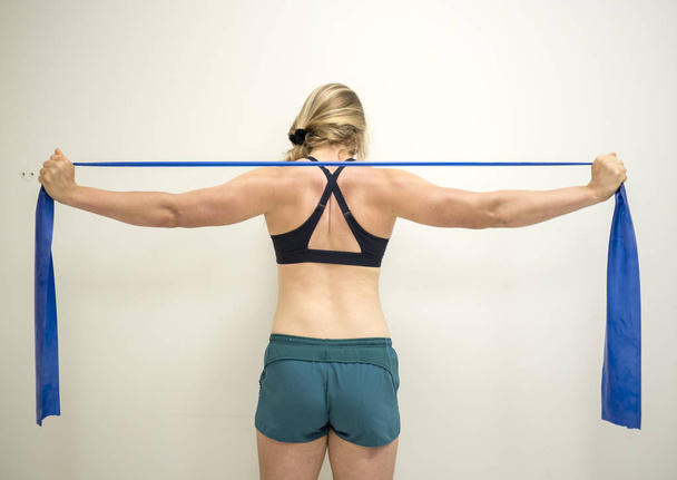 Сильная спортсменка с помощью терабанда сопротивления укрепляет мышцы рук
 - Фото, изображение