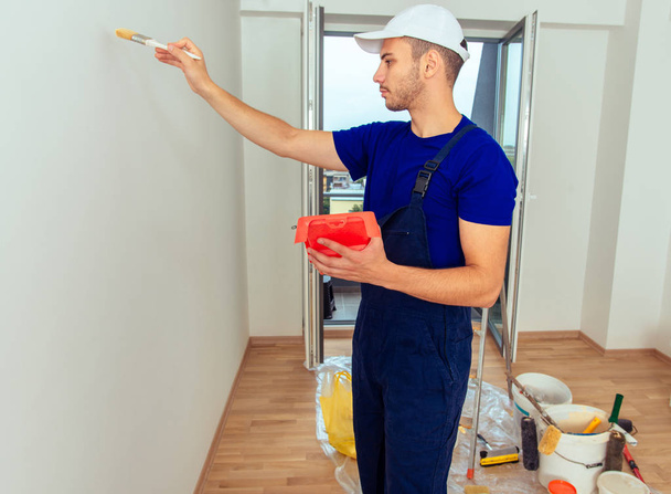 Веселий живописець у синьому загальному ремонті своєї кімнати під час малювання стіни
 - Фото, зображення