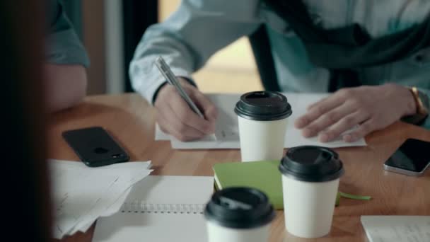 Mãos masculinas de membros da equipe tomando notas sobre o plano de trabalho de papel usando reunião de equipe de caneta e brainstorming
 - Filmagem, Vídeo