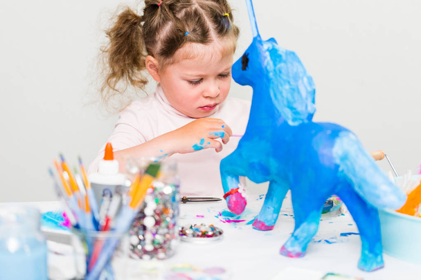 Маленька дівчинка прикрашає пофарбований блакитний папір Маха єдиноріг
. - Фото, зображення