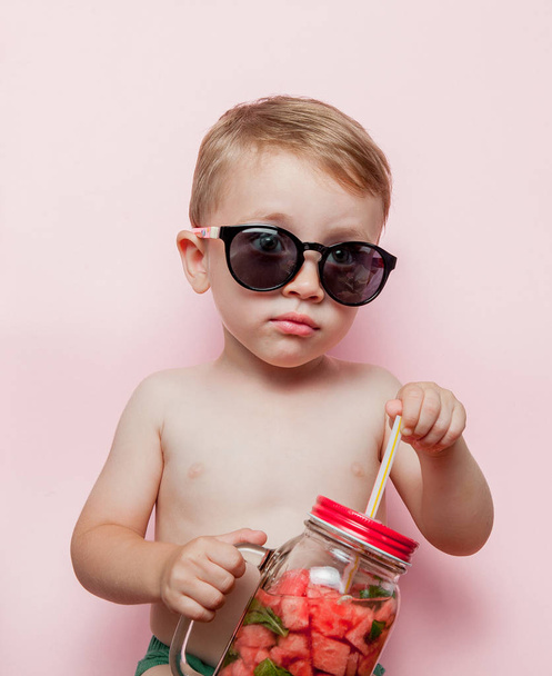 Little boy with Jar of cold fresh lemonade with piece of watermelon and ice on pink background. - Фото, зображення