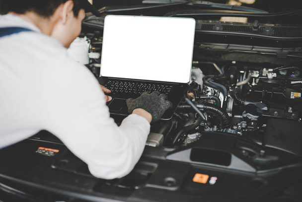Young men mechanic working on a computer connected to a car engine. Mockup computer - Photo, Image