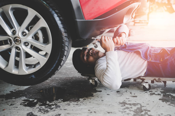 Young mechanic lying down and working under car at the garage.  Repair undercarriage service. - Foto, Imagem
