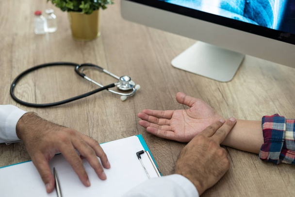 Hand eines Arztes, der den Puls eines männlichen Patienten an einem Schreibtisch im Krankenhaus überprüft. - Foto, Bild