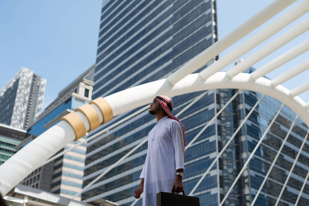 Mladý arabský obchodník drží ve městě tašku. v pozadí města Bangkok, obchodní čtvrti s vysokou budovou oslnil - Fotografie, Obrázek