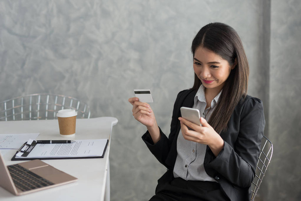 Aziatische business meisje in haar werkstation online met een credit card en slimme telefoon kopen. Online winkelen Concept - Foto, afbeelding