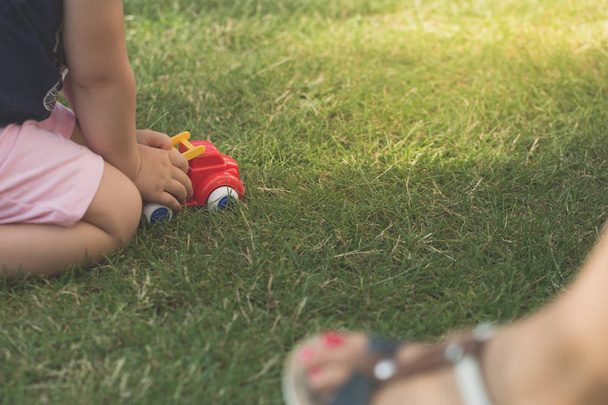 Маленька дівчинка грає червону машину в садовій траві
. - Фото, зображення