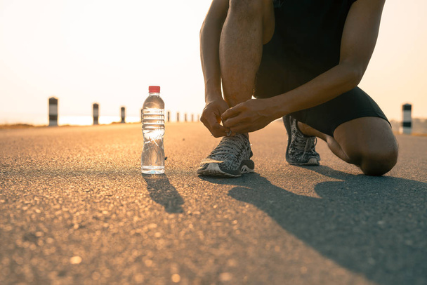 Male runner tying shoes in preparation for a run in the morning and bottle water. The concept of health and fitness - Photo, Image