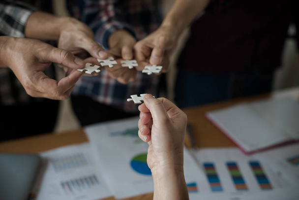 Hands group of business people assembling jigsaw puzzle white. Below is the graph paper business documents placed on a wooden table in the meeting room. - Photo, Image