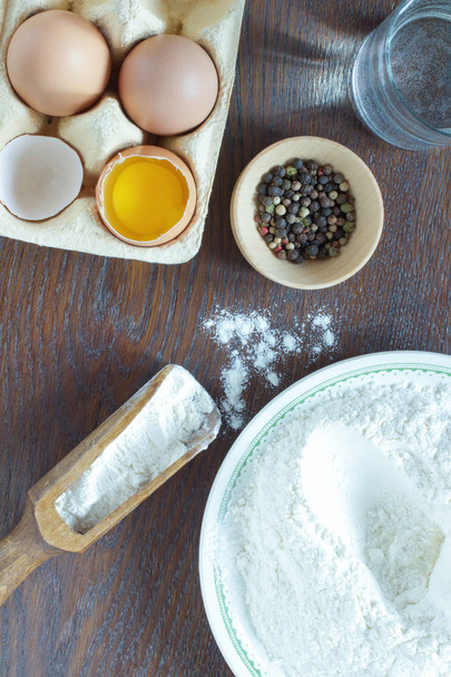 Flour in a bowl and a wooden spoon. Chicken eggs. Glass of water - Foto, immagini