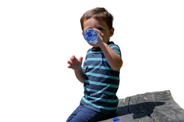 Διψασμένος μικρό αγόρι κάθεται σε ένα ξύλινο πάγκο και το πόσιμο νερό. - Φωτογραφία, εικόνα