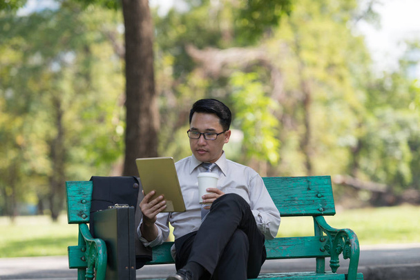Biznesmen sit wyboru e-mail na cyfrowy tablet w ogrodzie w drodze powrotnej do domu. - Zdjęcie, obraz